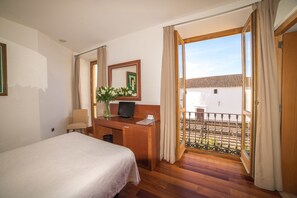 A hotel room with a bed, a desk with a computer, a mirror, and a view of a courtyard.