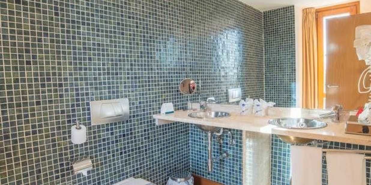 A bathroom with blue mosaic tiles, two sinks, a mirror, and a towel rack.