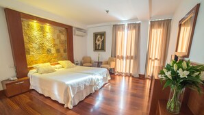 Habitación de hotel con una cama grande, dos sillones, una mesita y un florero.