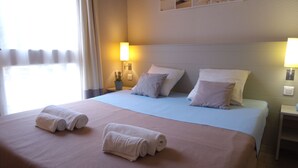 A hotel room with a large bed, two bedside lamps, and a window with curtains. - VVF Île de Ré Sainte-Marie-de-Ré (Sainte-Marie-de-Re)