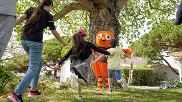 Un groupe de personnes interagissant avec une grande mascotte orange dans un espace extérieur résidentiel.