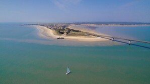 An aerial view of a coastal area with a bridge, sandy beach, and a sailboat. - VVF Île de Ré Sainte-Marie-de-Ré (Sainte-Marie-de-Re)