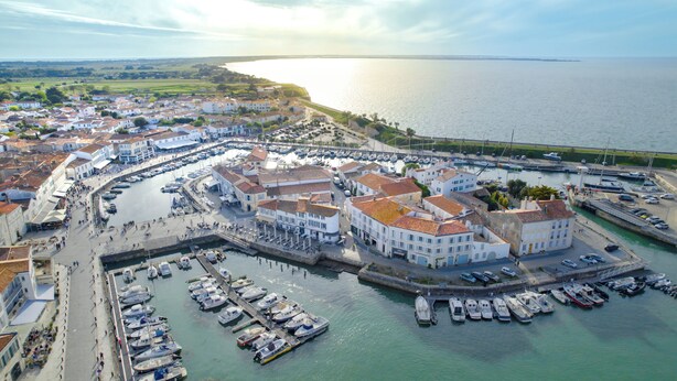 An aerial view of a coastal town with a marina, buildings with red-tiled roofs, and a large body of water. - VVF Île de Ré Sainte-Marie-de-Ré (Sainte-Marie-de-Re)