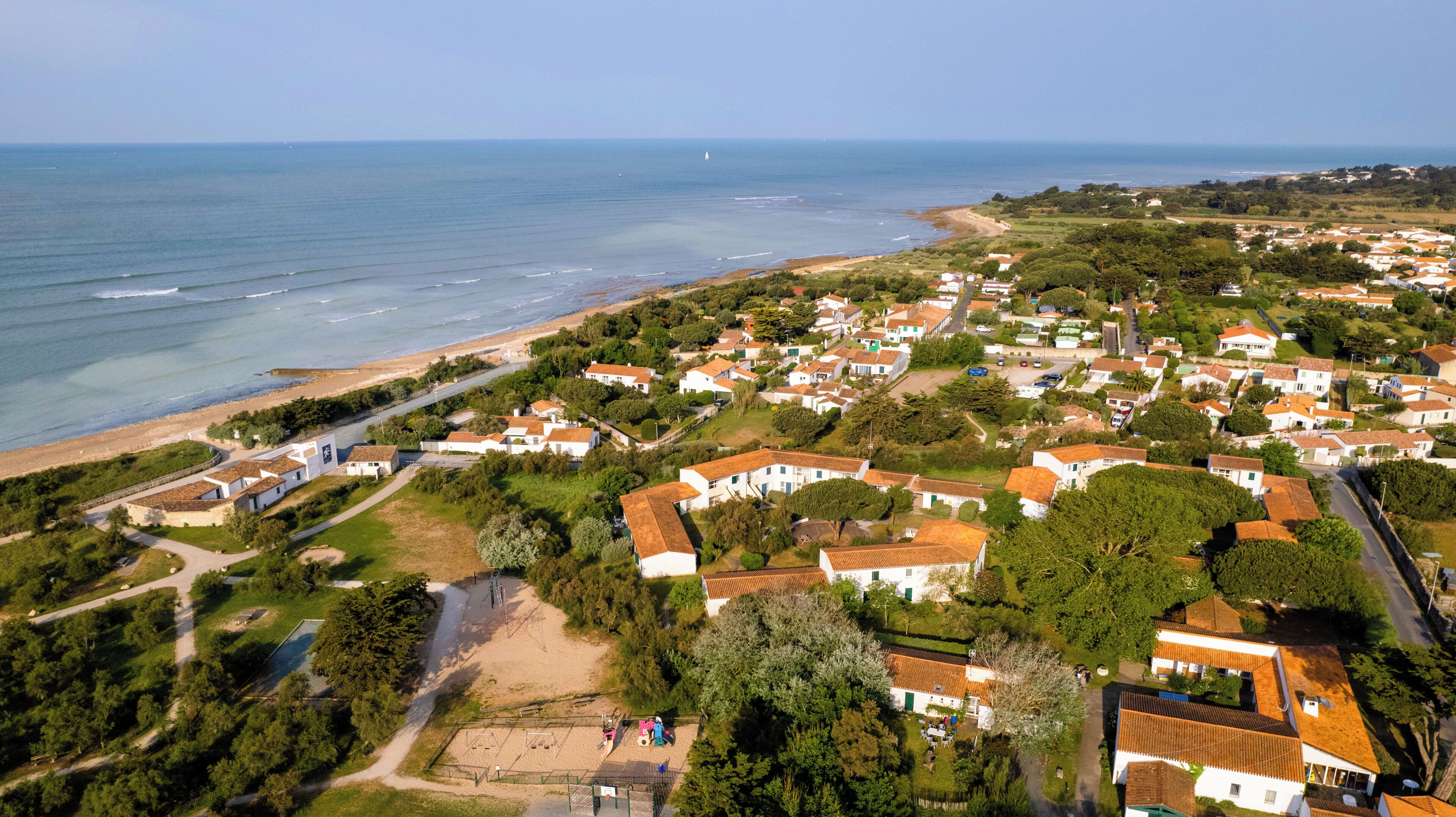 Luchtbeeld van een kustgebied met huizen, een strand en een heldere lucht.