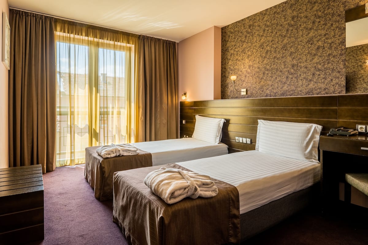 A hotel room with two beds, a desk, and a large window with curtains.