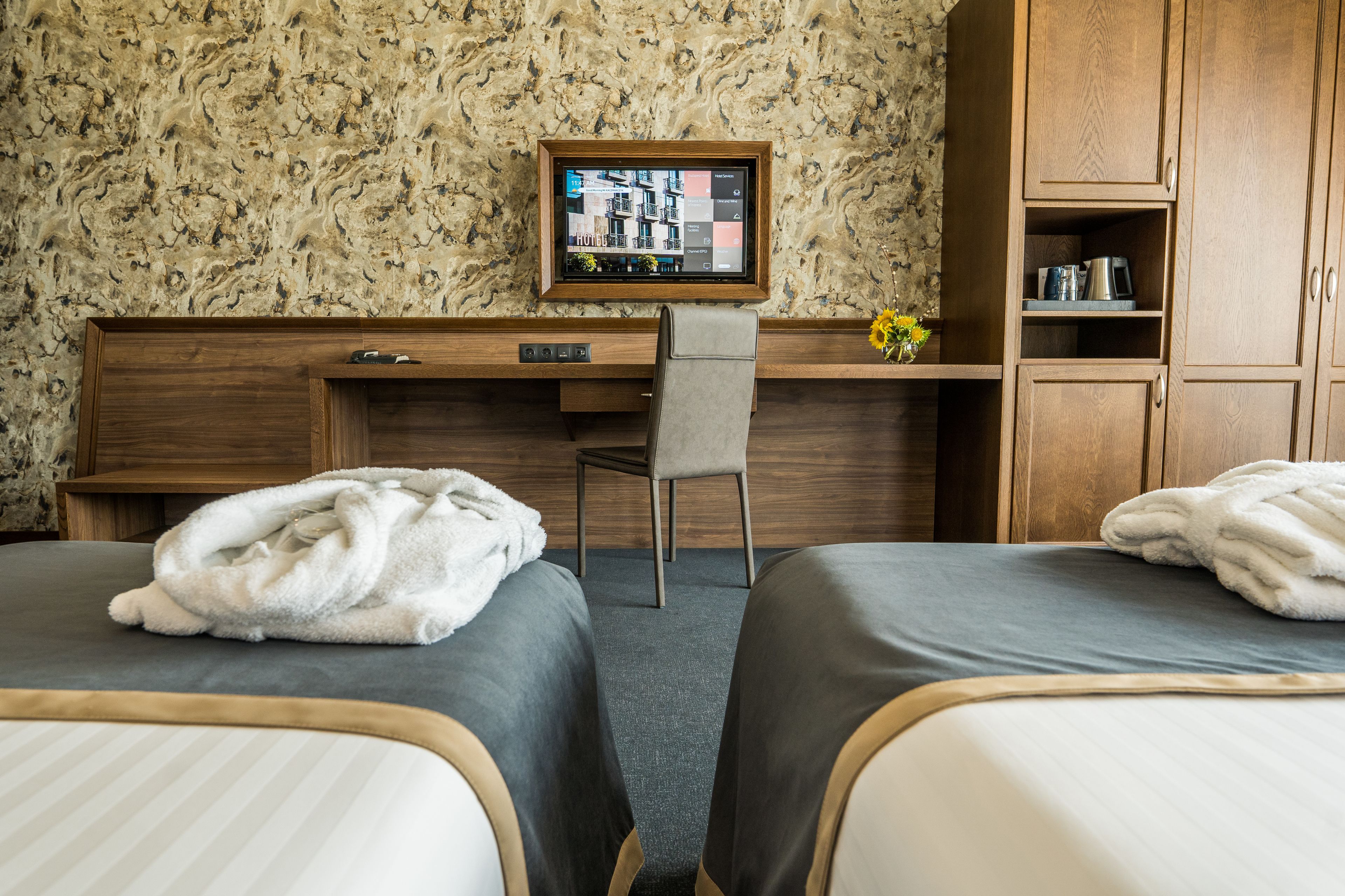 A hotel room with two beds, a desk, a chair, and a TV mounted on the wall.