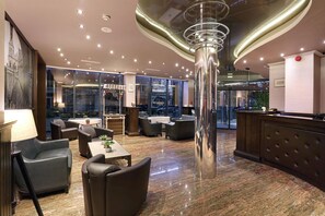 A modern lobby with a central column, seating areas, and a reception desk. - Hotel Budapest (Sofia)