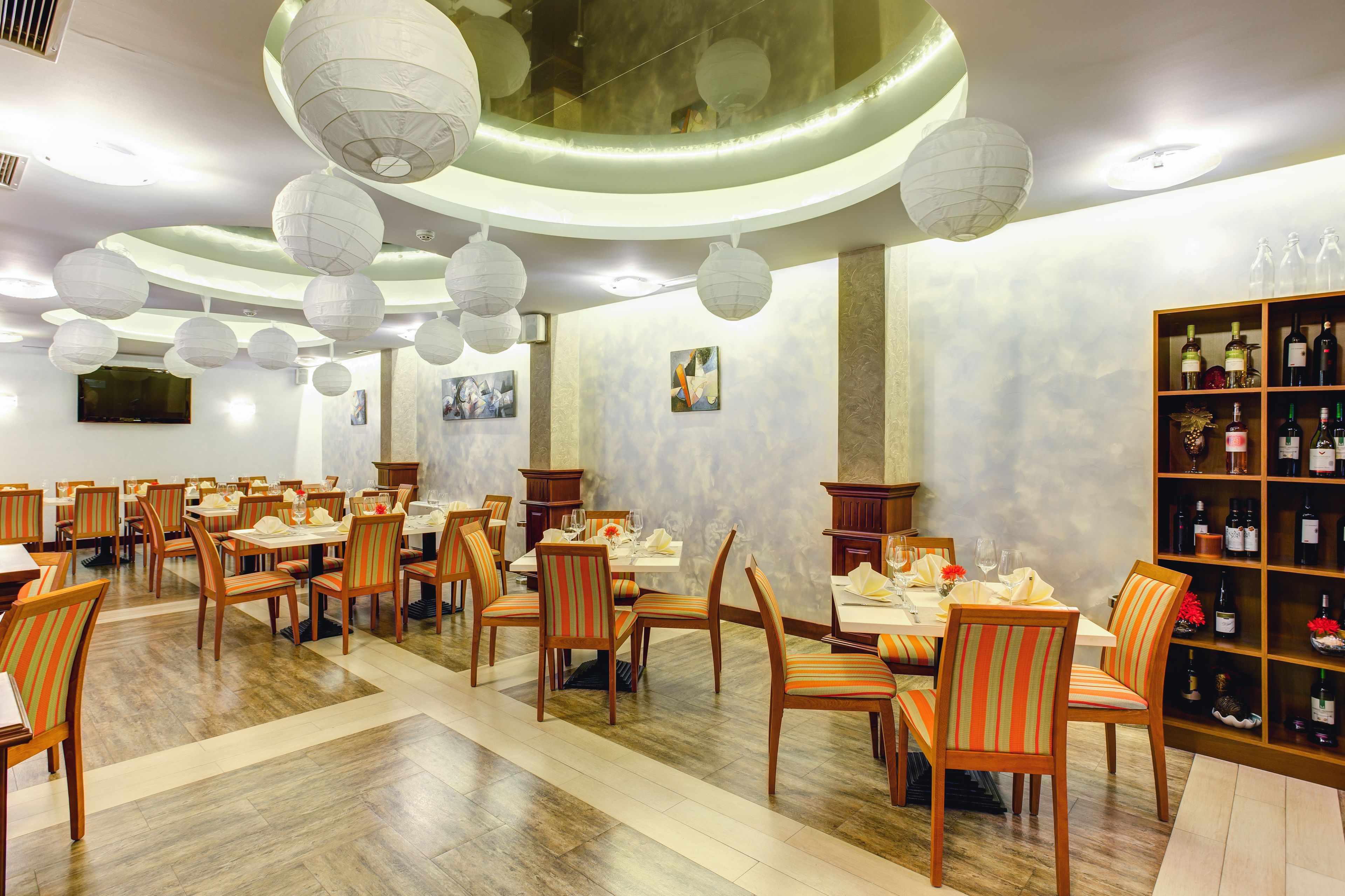 Un restaurante con varias mesas y sillas, una estantería para vinos y farolillos decorativos en el techo.