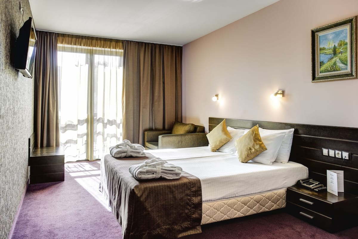 A hotel room with a bed, a sofa, a TV, and a painting on the wall.
