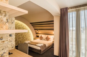 Una habitación de hotel moderna con una pared de acento de piedra, un techo curvo, una cama con cabecera de madera y un amplio ventanal con cortinas.