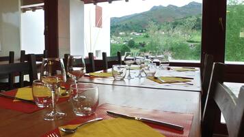Une table à manger dressée avec des verres à vin, des couverts et des serviettes, offrant une vue pittoresque sur des maisons et des collines.