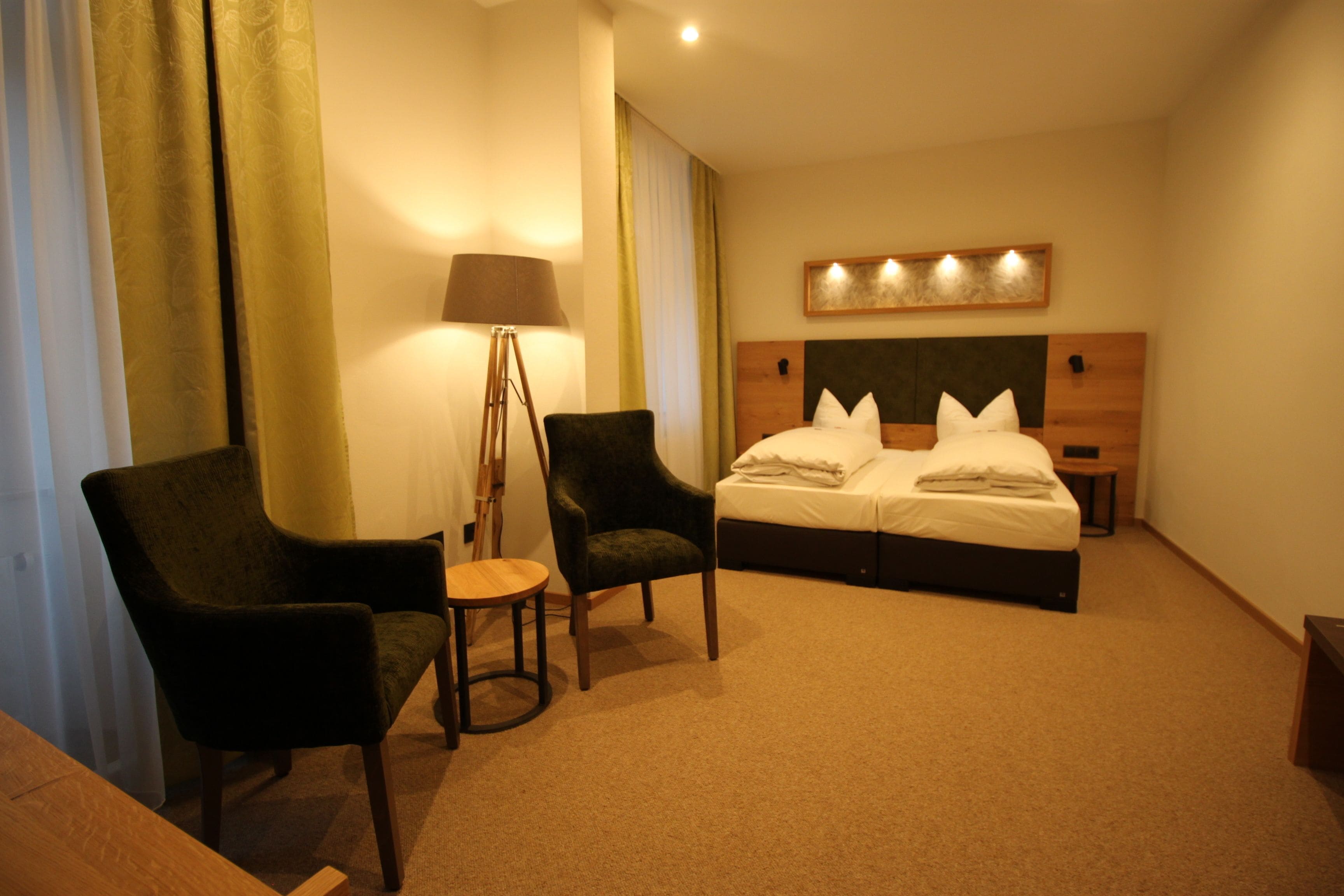 Ein Hotelzimmer mit einem Bett, zwei Sesseln, einem kleinen Tisch, einer Lampe und einer Wandleuchte.