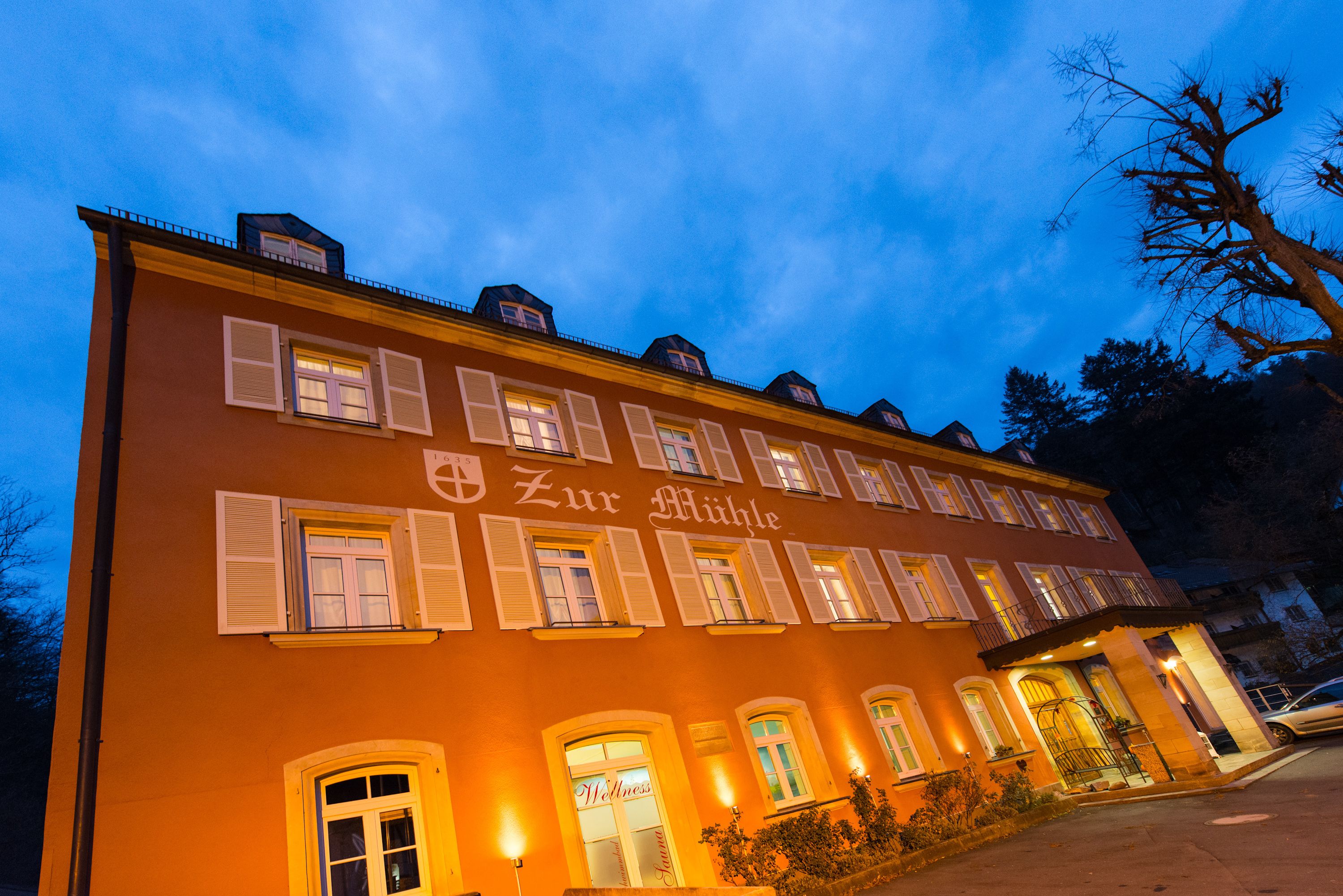 A multi-story building with a sign reading "Zur Mühle" and multiple windows with shutters.