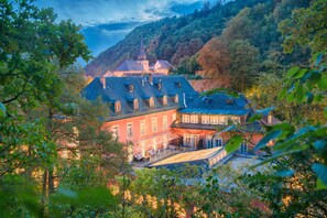 A traditional European-style building with multiple windows and a prominent tower, surrounded by lush greenery. - Hotel Hartl's Lindenmühle (Bad Berneck im Fichtelgebirge)