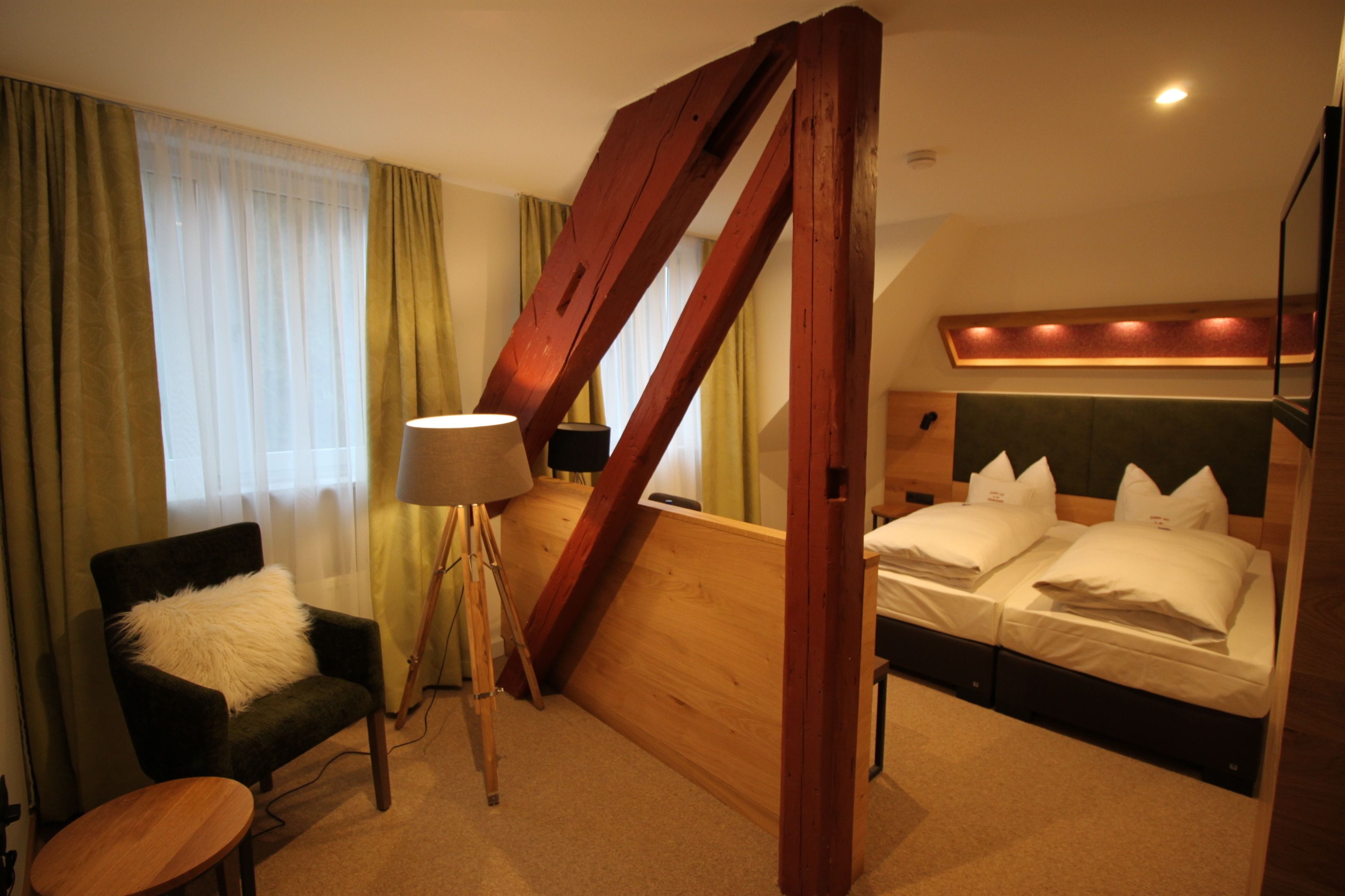 Una habitación con cama, una silla, una lámpara y estructura de vigas de madera.