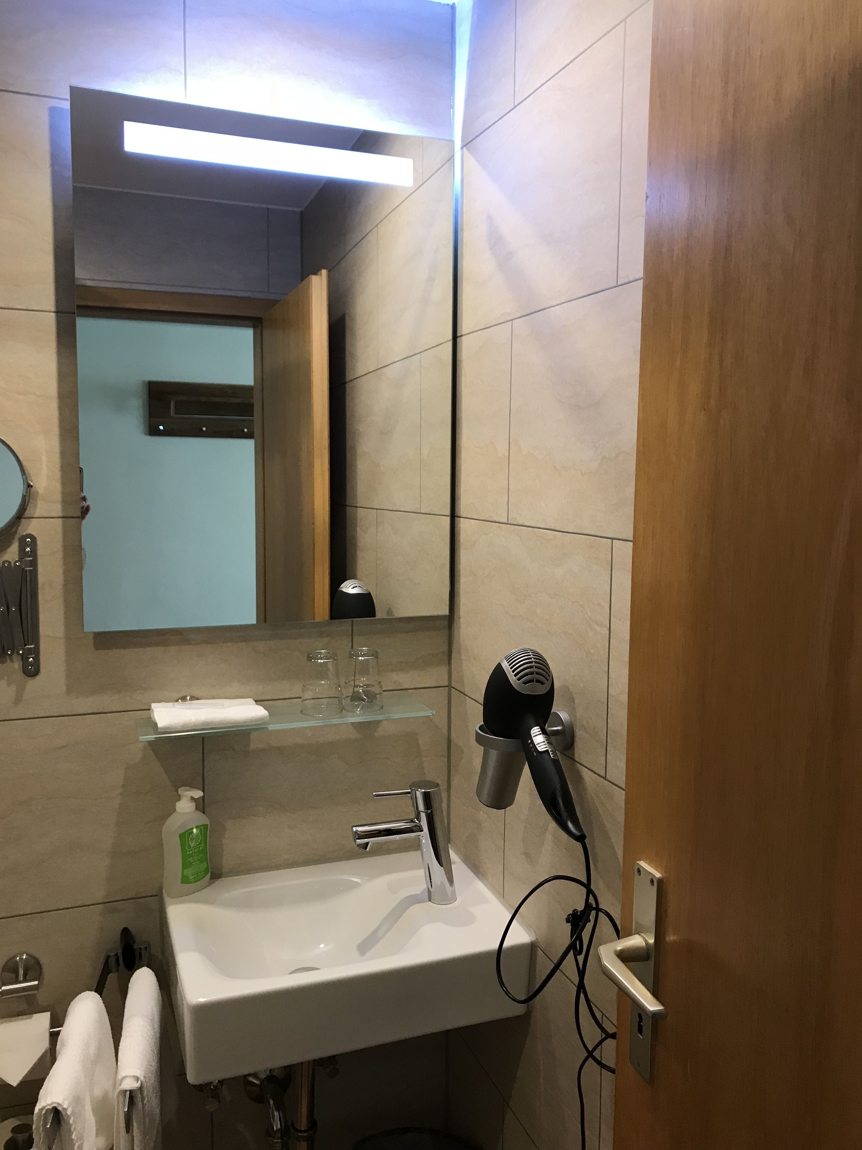 A modern bathroom with a white sink, a mirror, a hairdryer, and a towel rack.