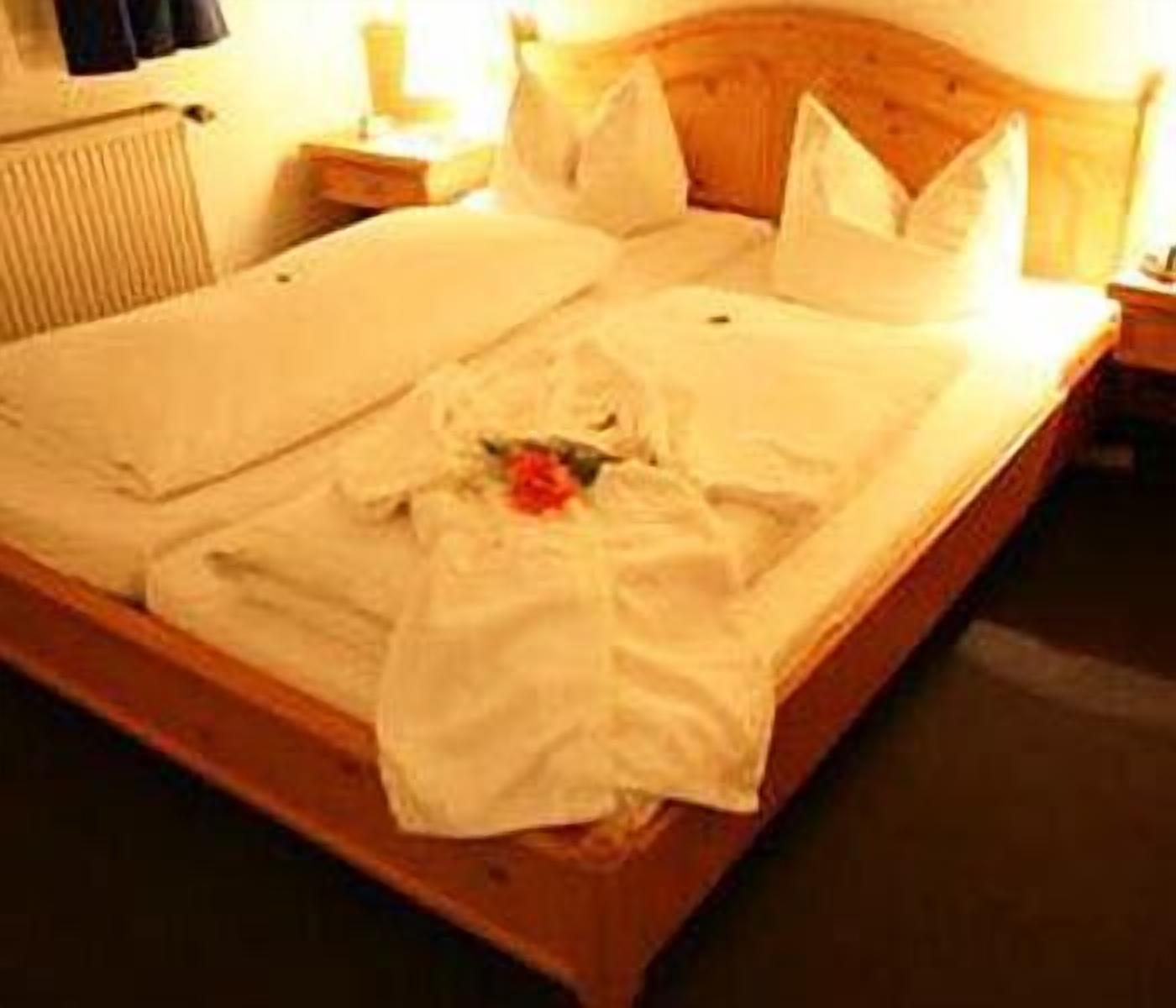A neatly made bed with white linens and a single red rose.