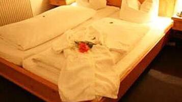 A neatly made bed with white linens and a single red rose.