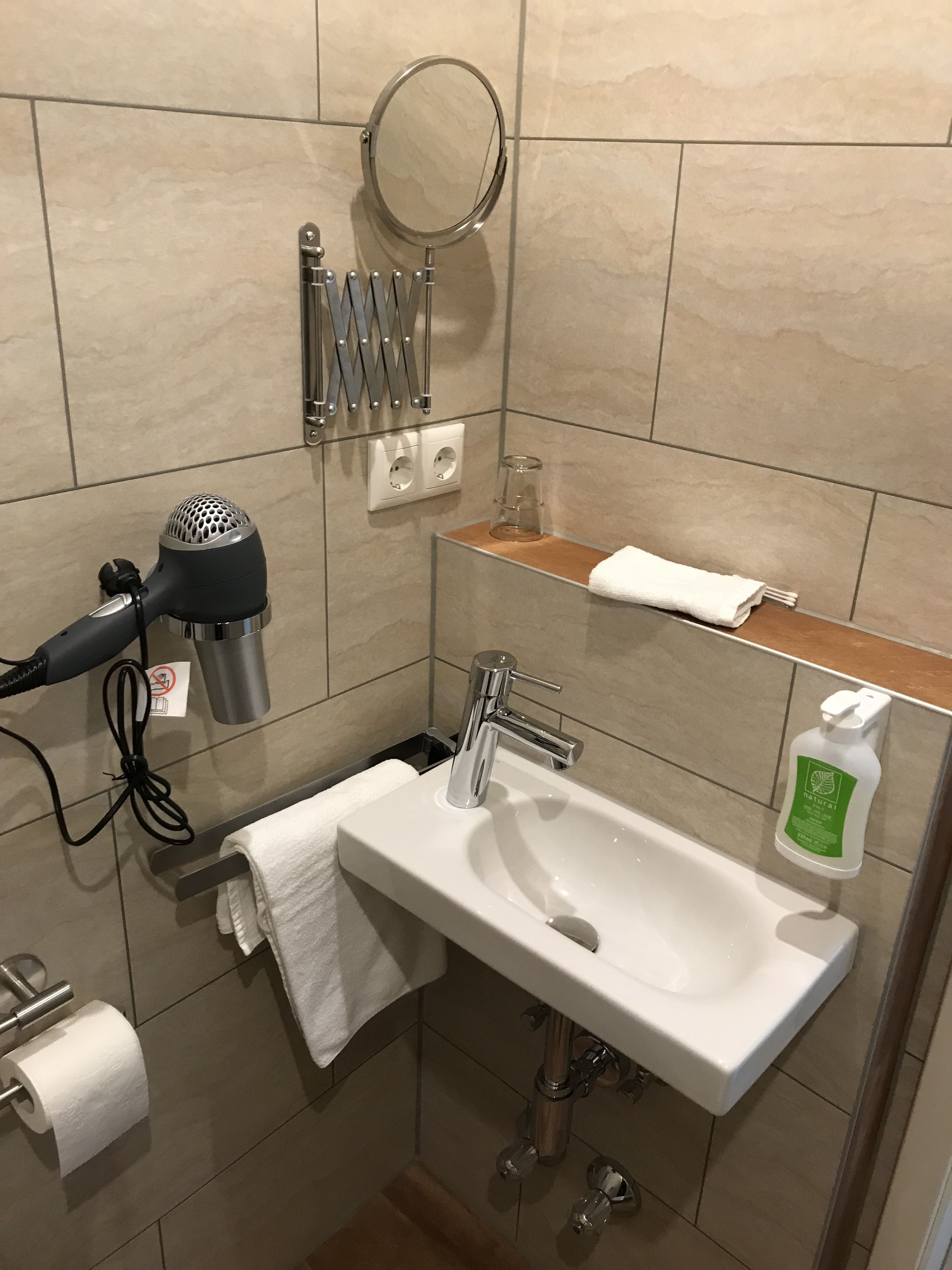 Casa de banho com lavatório, espelho, porta-toalhas, secador de cabelo e artigos de higiene pessoal.