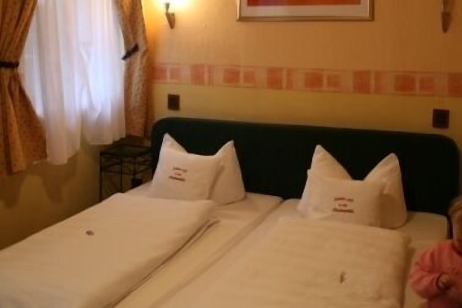 A hotel room with two single beds, each with a pillow and a blanket.