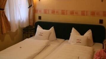 A hotel room with two single beds, each with a pillow and a blanket.