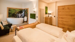 Ein modernes Hotelzimmer mit einem großen Bett, einer Sitzecke mit Sessel und kleinem Tisch, einem Holzschrank und einem großen Wandbild eines Wasserfalls.