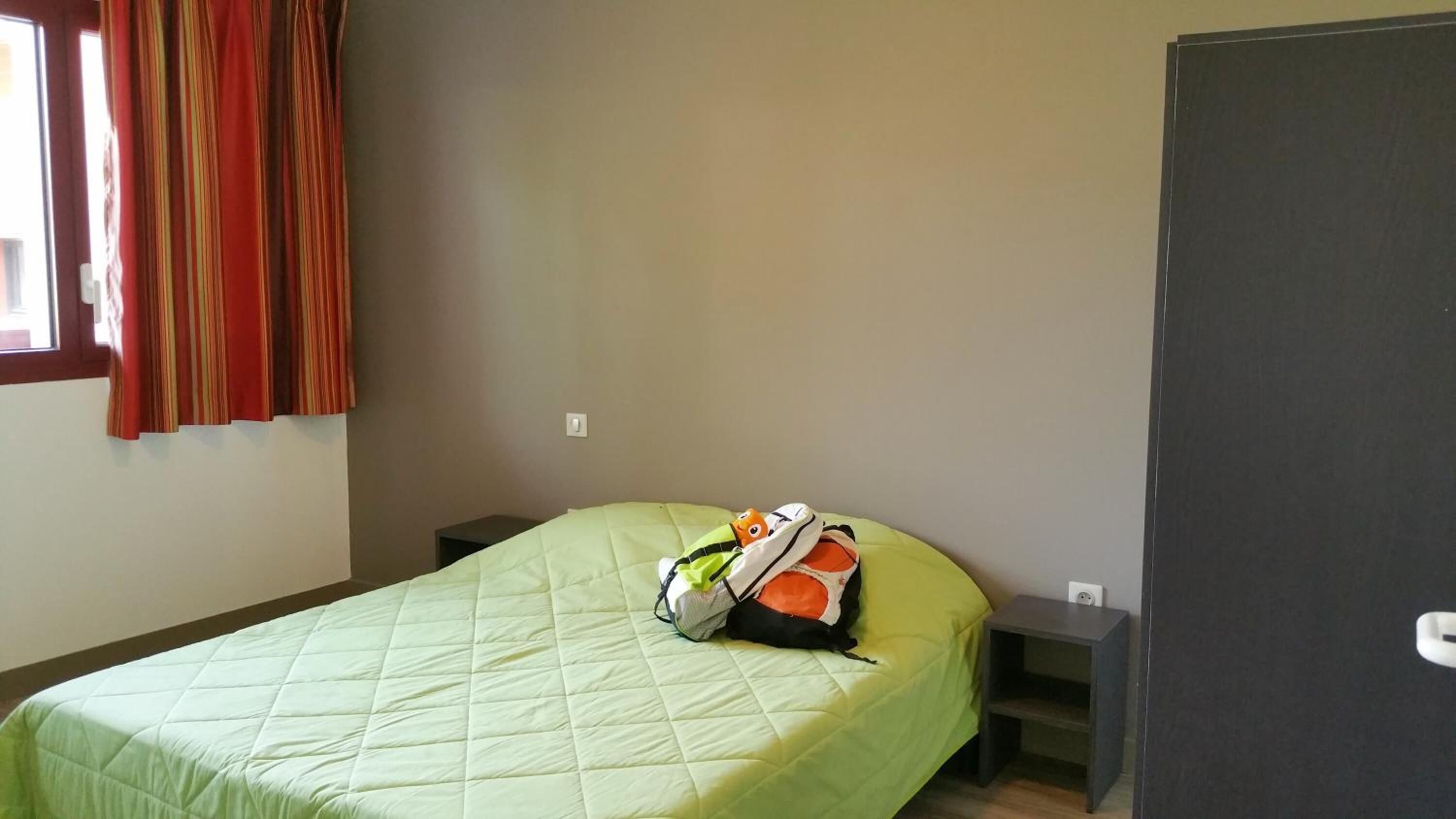 A single bed with a green quilt, a small bedside table, and a nightstand.