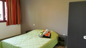 A single bed with a green quilt, a small bedside table, and a nightstand.