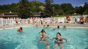 A swimming pool with people in the water, a white fence, and buildings in the background. - VVF Haute Loire Saint-Julien-Chapteuil (Saint-Julien-Chapteuil)