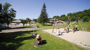 A playground with swings and a seesaw, surrounded by grass and trees. - VVF Haute Loire Saint-Julien-Chapteuil (Saint-Julien-Chapteuil)