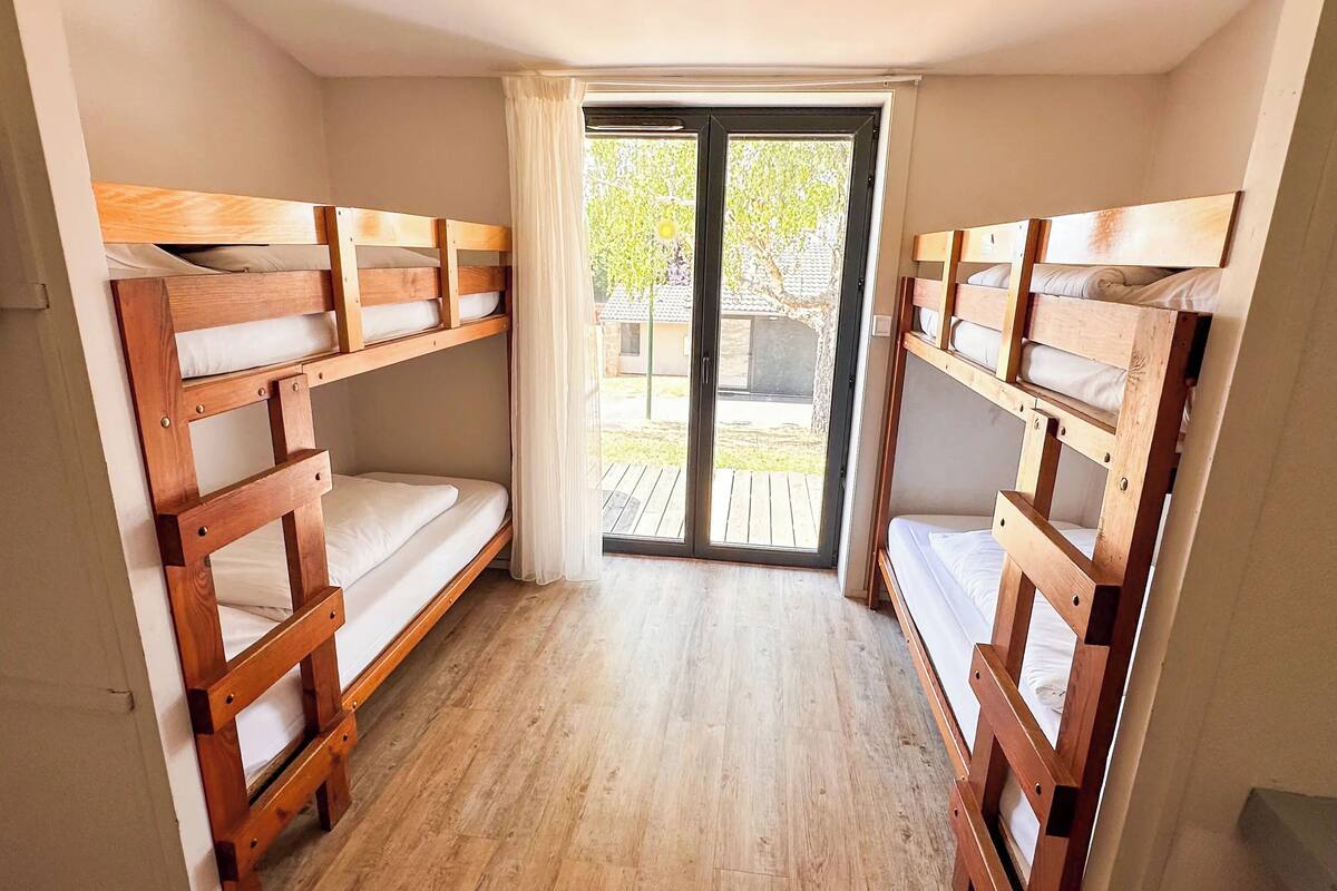 A room with two wooden bunk beds, a sliding glass door leading to an outdoor area, and a wooden floor.