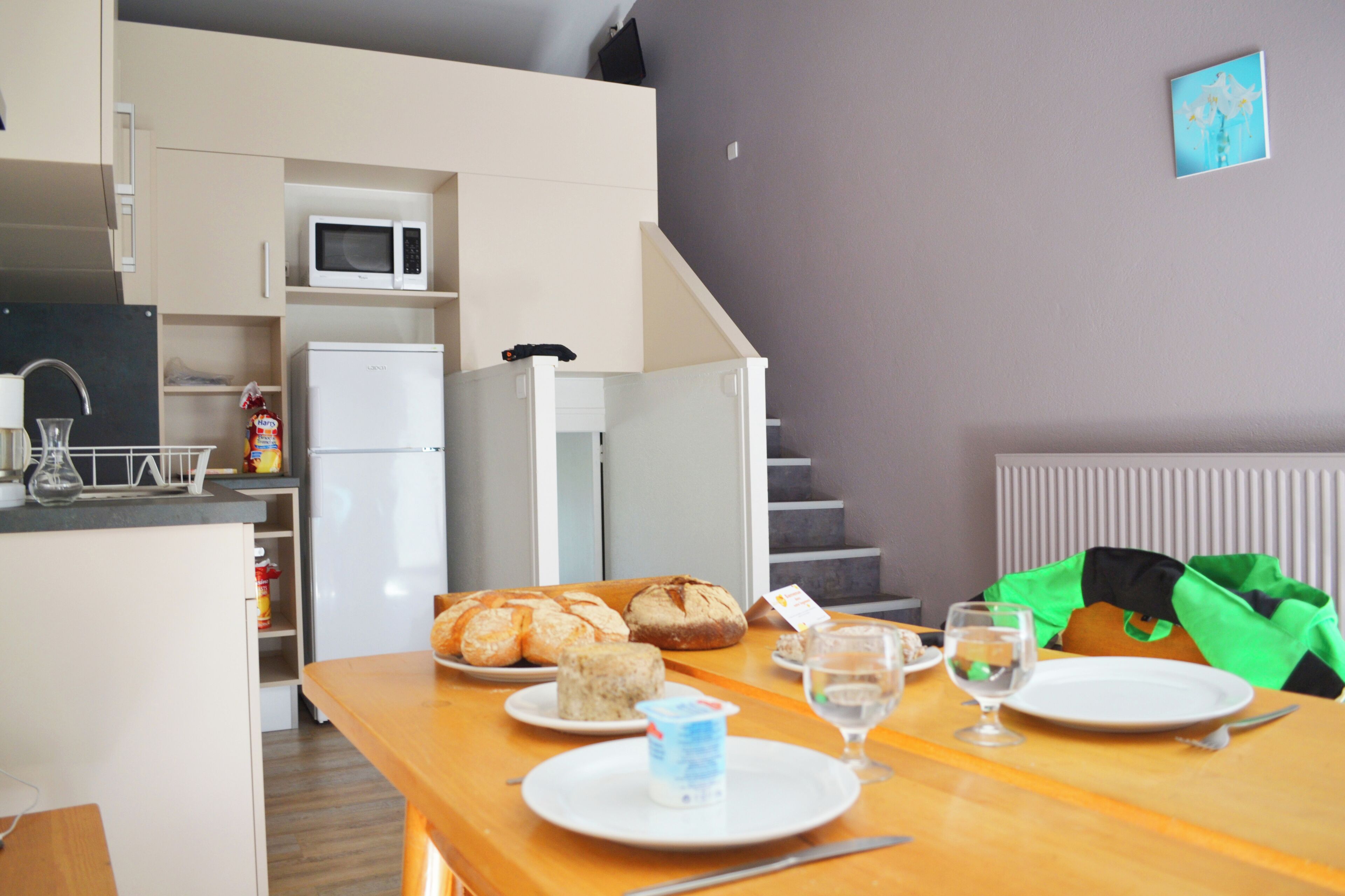 Una cocina compacta con microondas, refrigerador y comedor con pan y un vaso de agua en la mesa.