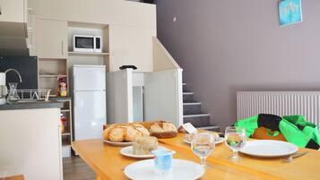 Una cocina compacta con microondas, refrigerador y comedor con pan y un vaso de agua en la mesa.