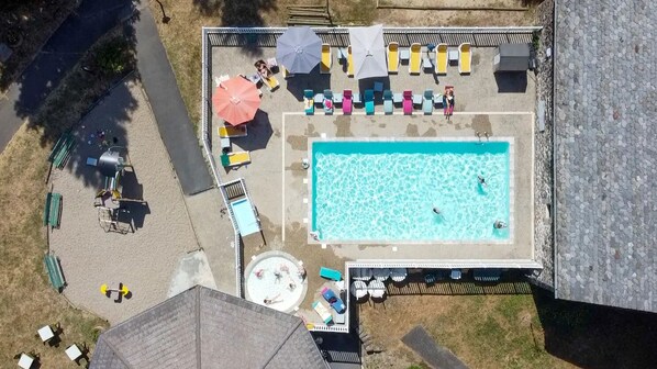 Vue aérienne d’un espace piscine comprenant des chaises longues, des parasols et une petite piscine circulaire pour enfants.