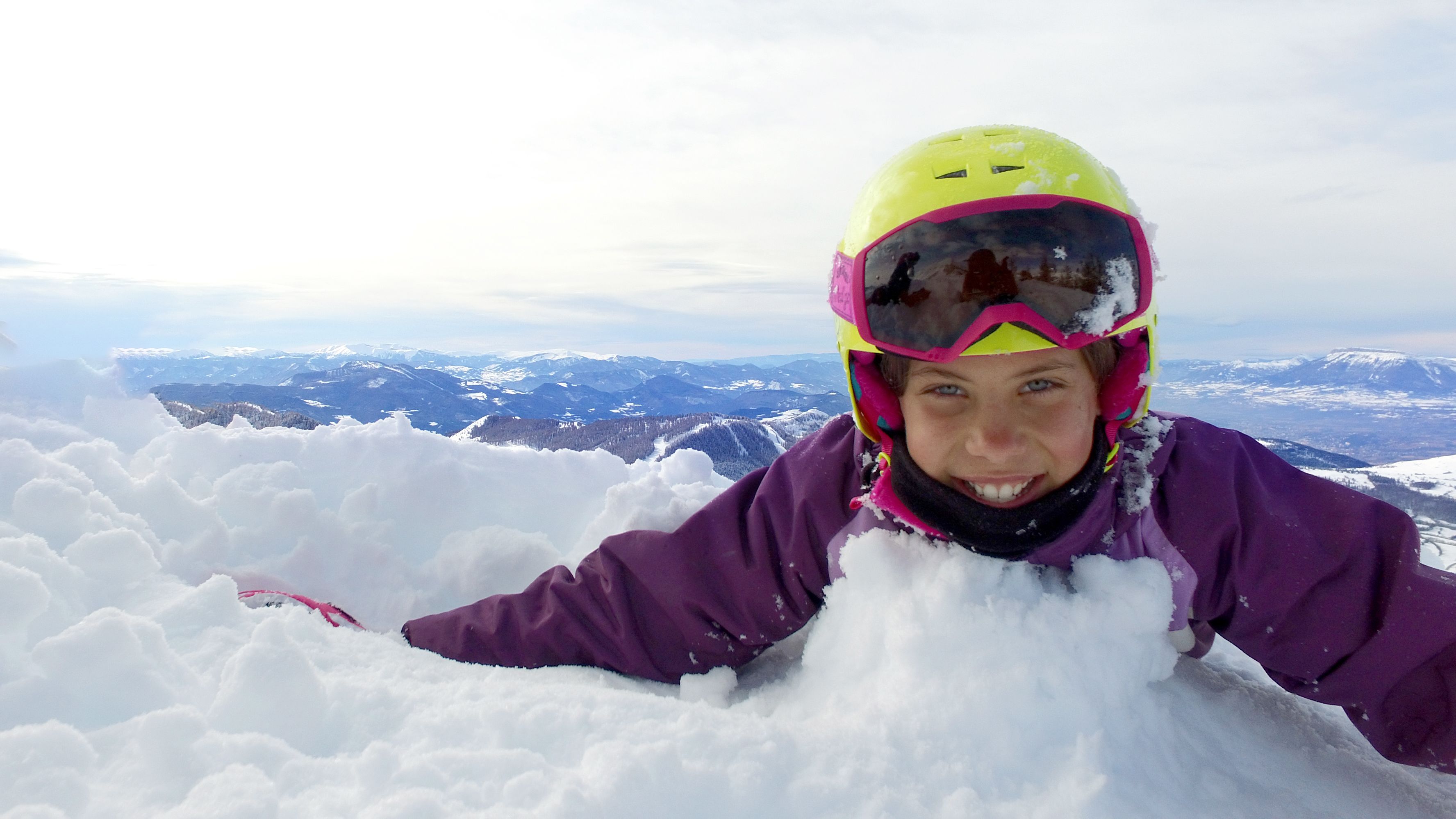 Una persona con un giubbotto viola e un elmetto giallo su una montagna innevata.