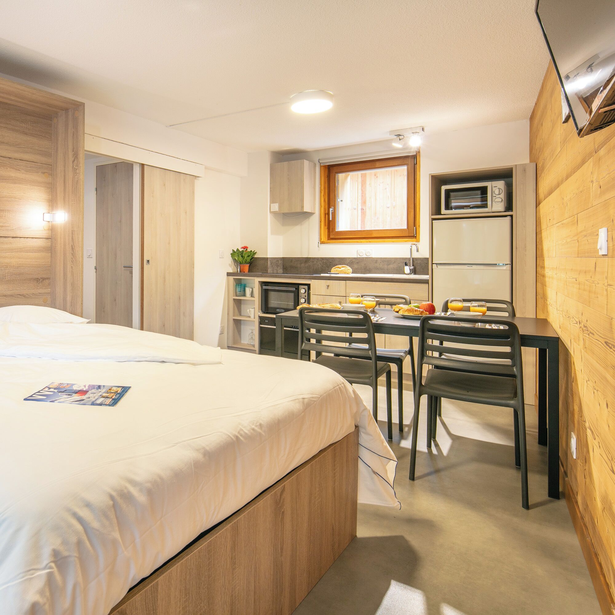 Una habitación de hotel compacta con una cama, kitchenette y comedor.