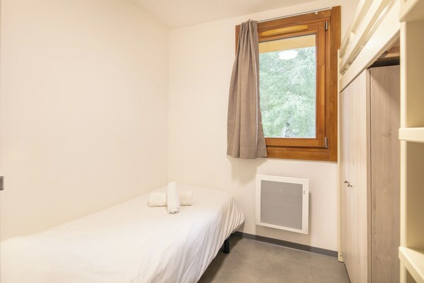 A small, single-bed room with a window, a radiator, and a wardrobe.
