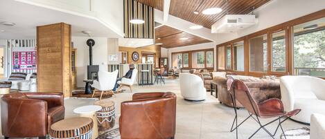 A spacious lobby with high ceilings, wooden beams, and large windows. There are multiple seating areas with leather and fabric furniture.