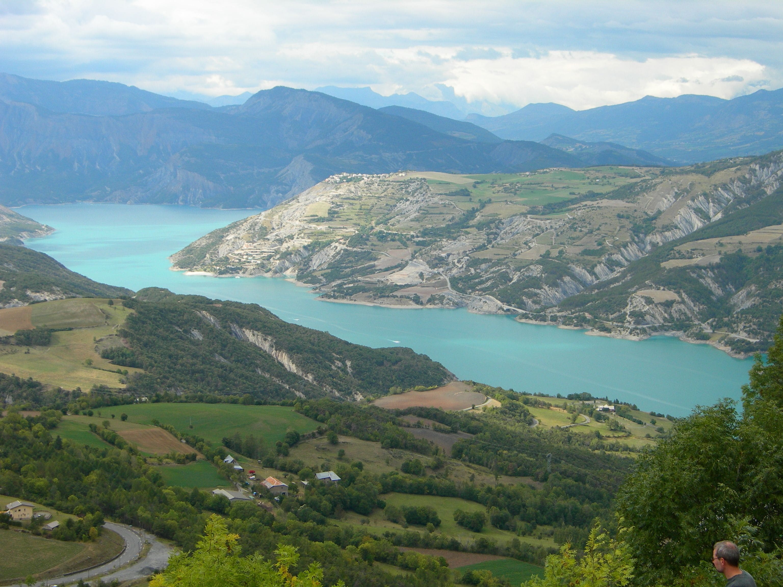 Un paysage montagneux avec un lac, des champs verdoyants et quelques bâtiments dispersés.