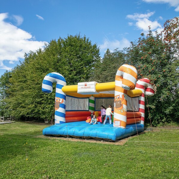 A colorful inflatable bounce house with cartoon characters, set in a grassy area with trees in the background.