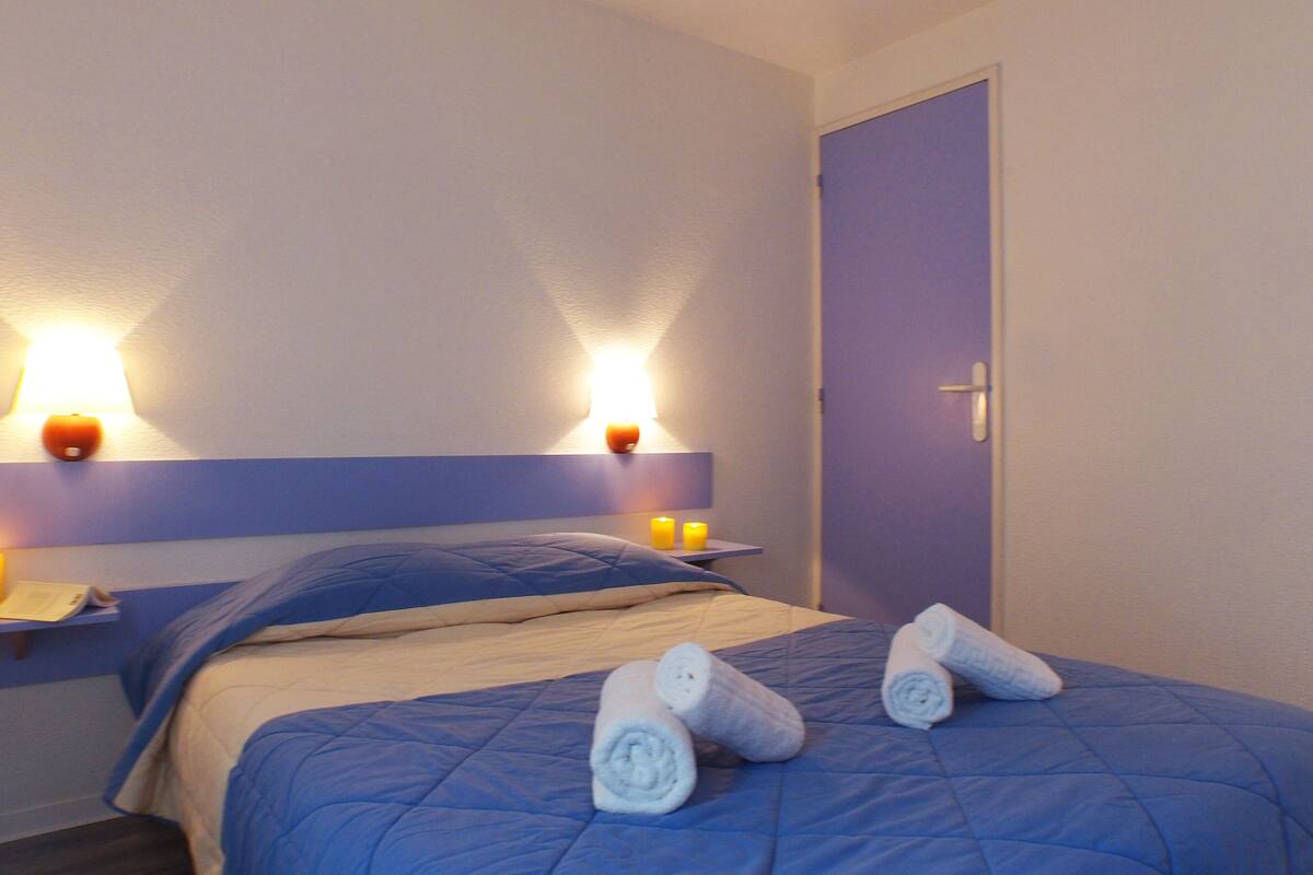 Ein Hotelzimmer mit einem Bett, zwei Wandlampen, einer Tür und zwei Handtüchern auf dem Bett.