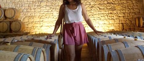 Una mujer camina por una bodega con paredes de piedra y barriles de madera.