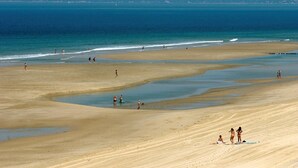 Een breed zandstrand met kalm water, enkele mensen wandelen en sommigen zitten op het zand.