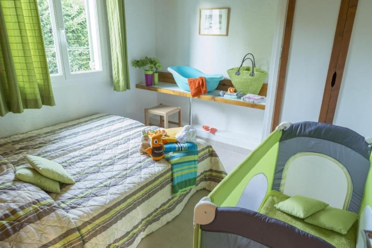Une chambre d’enfant avec un lit, un parc pour bébé et des étagères remplies de jouets et d’une plante.
