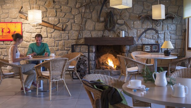 Un espacio al aire libre acogedor con sillas y mesas de mimbre, un muro de piedra de fondo y una chimenea.