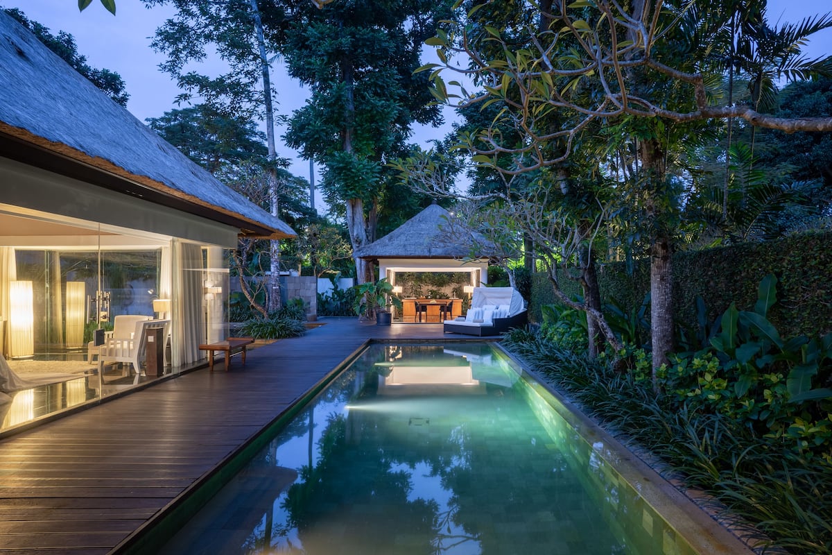 Uma casa moderna com piscina, deck de madeira e área de estar ao ar livre, rodeada por vegetação exuberante.