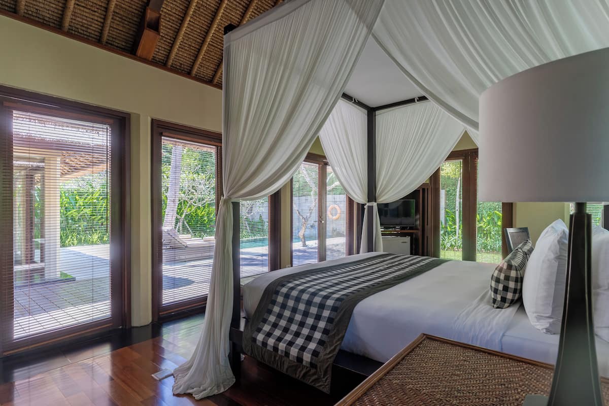 Quarto com cama grande, cortinas brancas e vista para o verde lá fora.