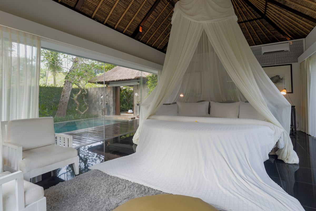 Quarto com cama de dossel, piscina fechada por vidro e vista para o exterior.
