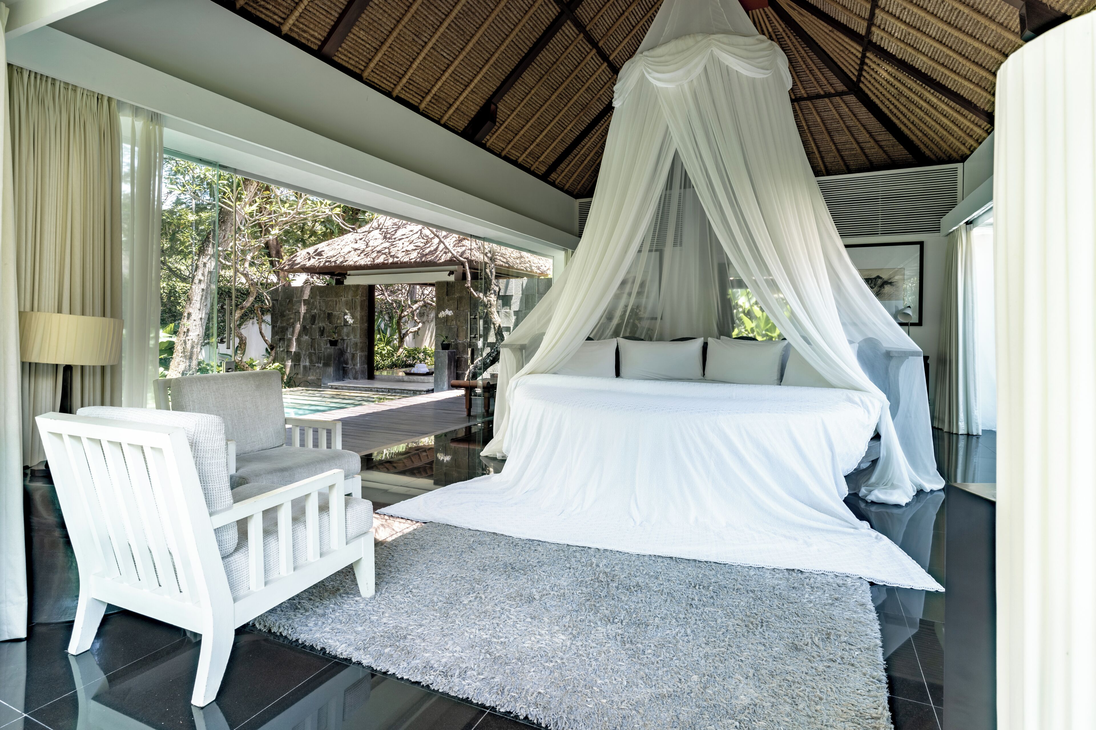 Ein Schlafzimmer mit Baldachinbett, einem weißen Stuhl und Blick ins Freie.