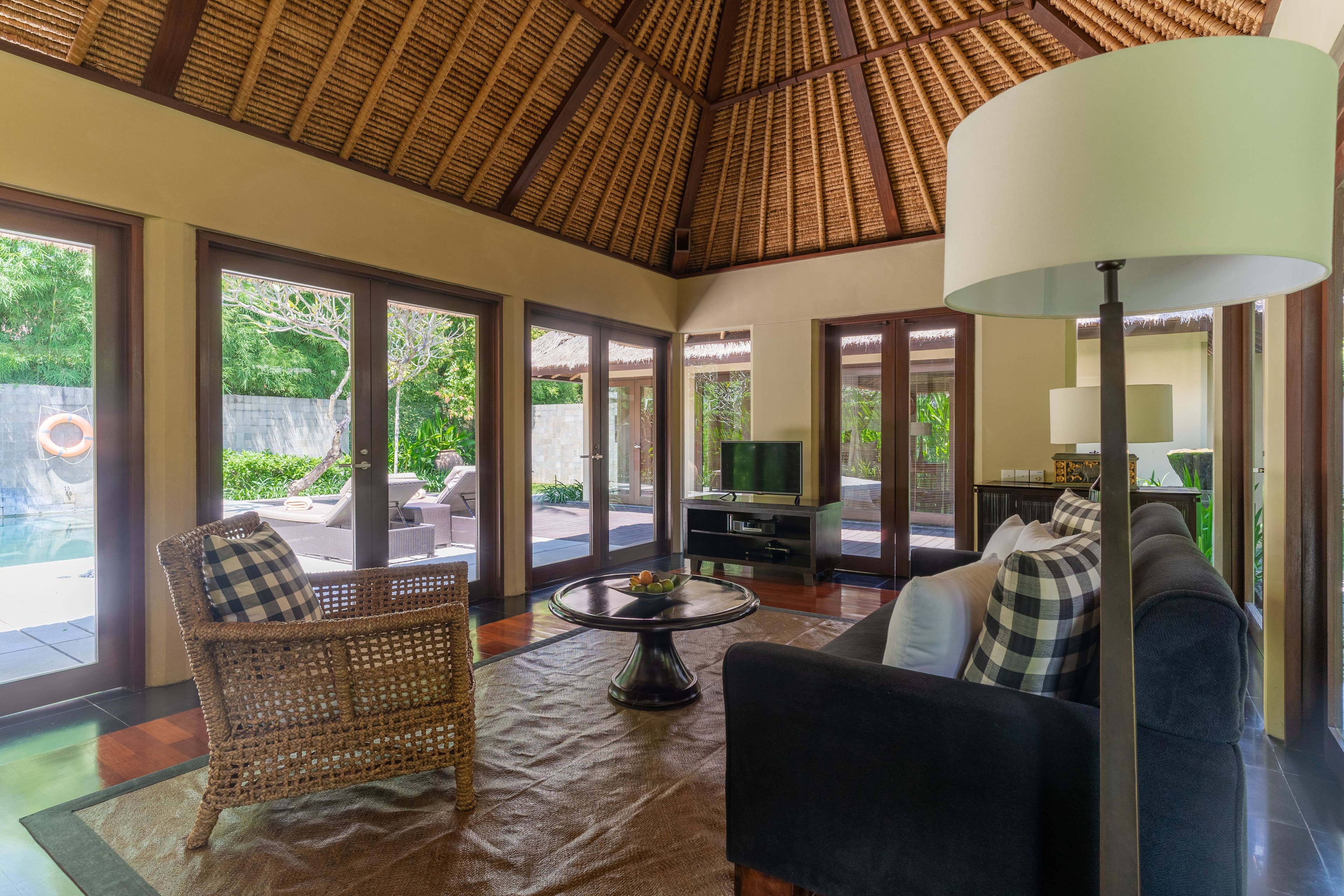 A spacious living area with a high thatched ceiling, wicker furniture, and a television.